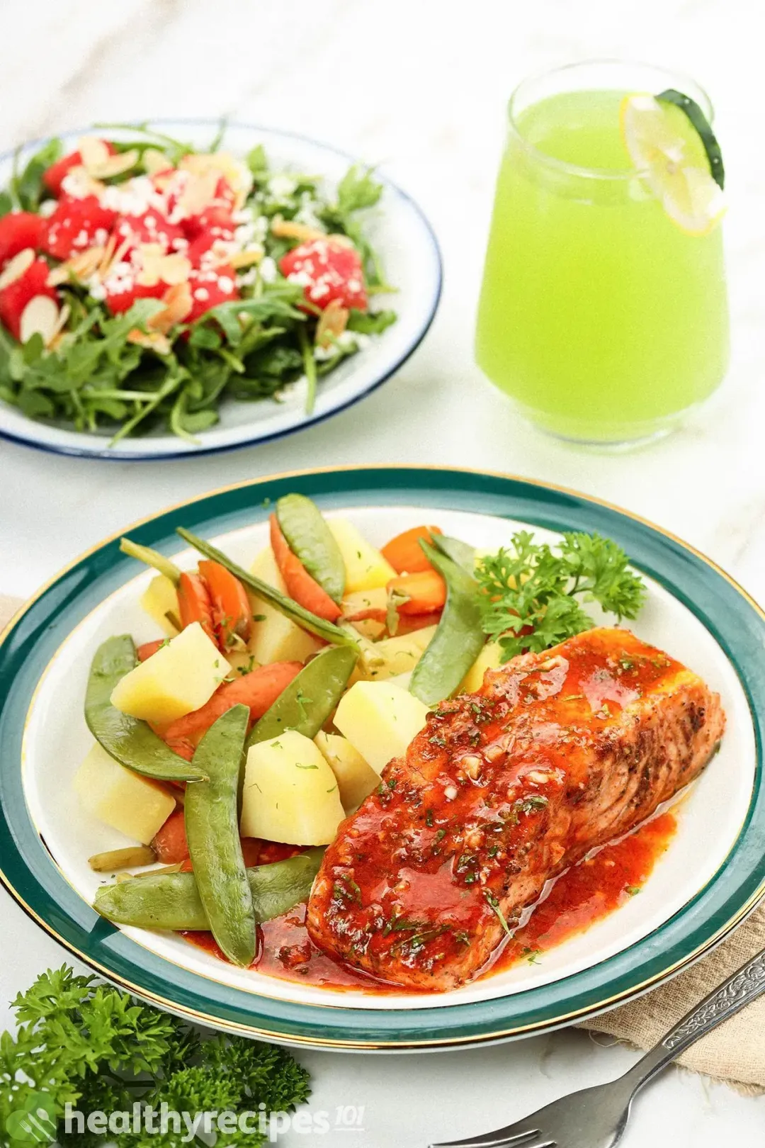A plate of Intant Pot salmon and vegetables with a plate of watermelon arugula salad and a glass of cucumber and lemon juice on the background