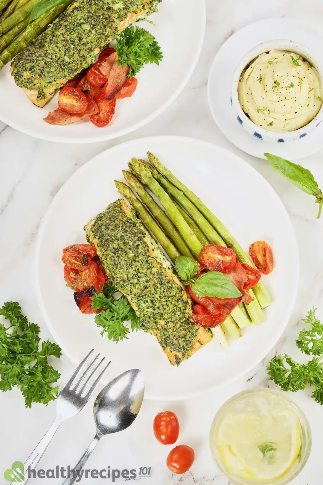 Two plates of salmon pesto surrounded with a glass of lemonade and a bowl of mashe potatoes