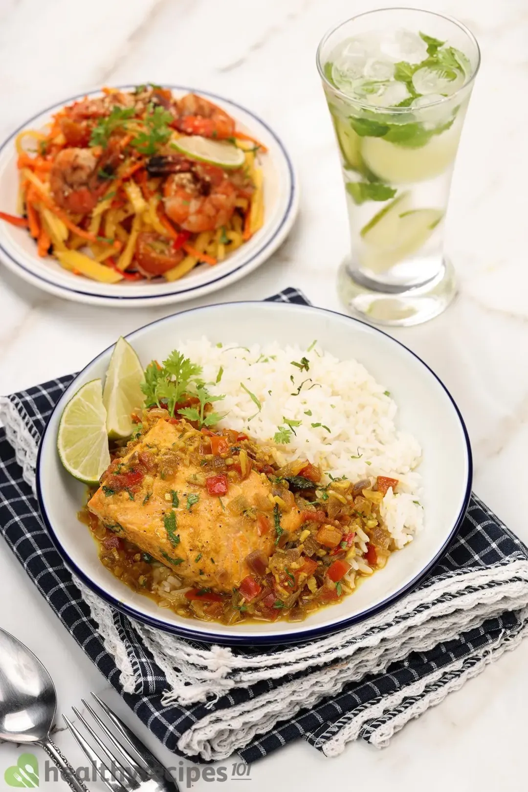 A plate of salmon curry and white rice laid on a dark blue tablecloth next to a glass of lime juice and some Thai salad