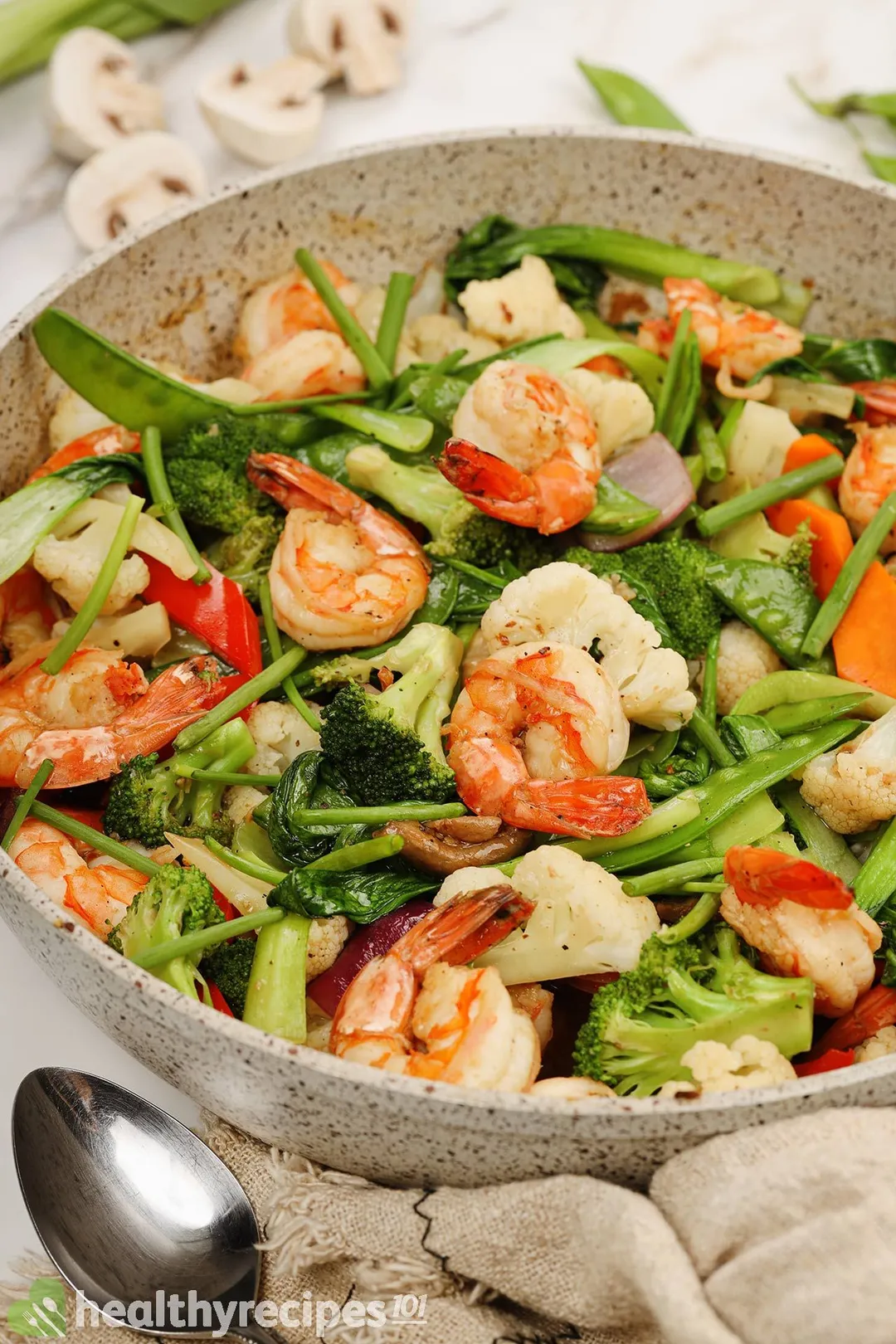 A non-stick pan full of shrimp chop suey with a metal spoon on the side.