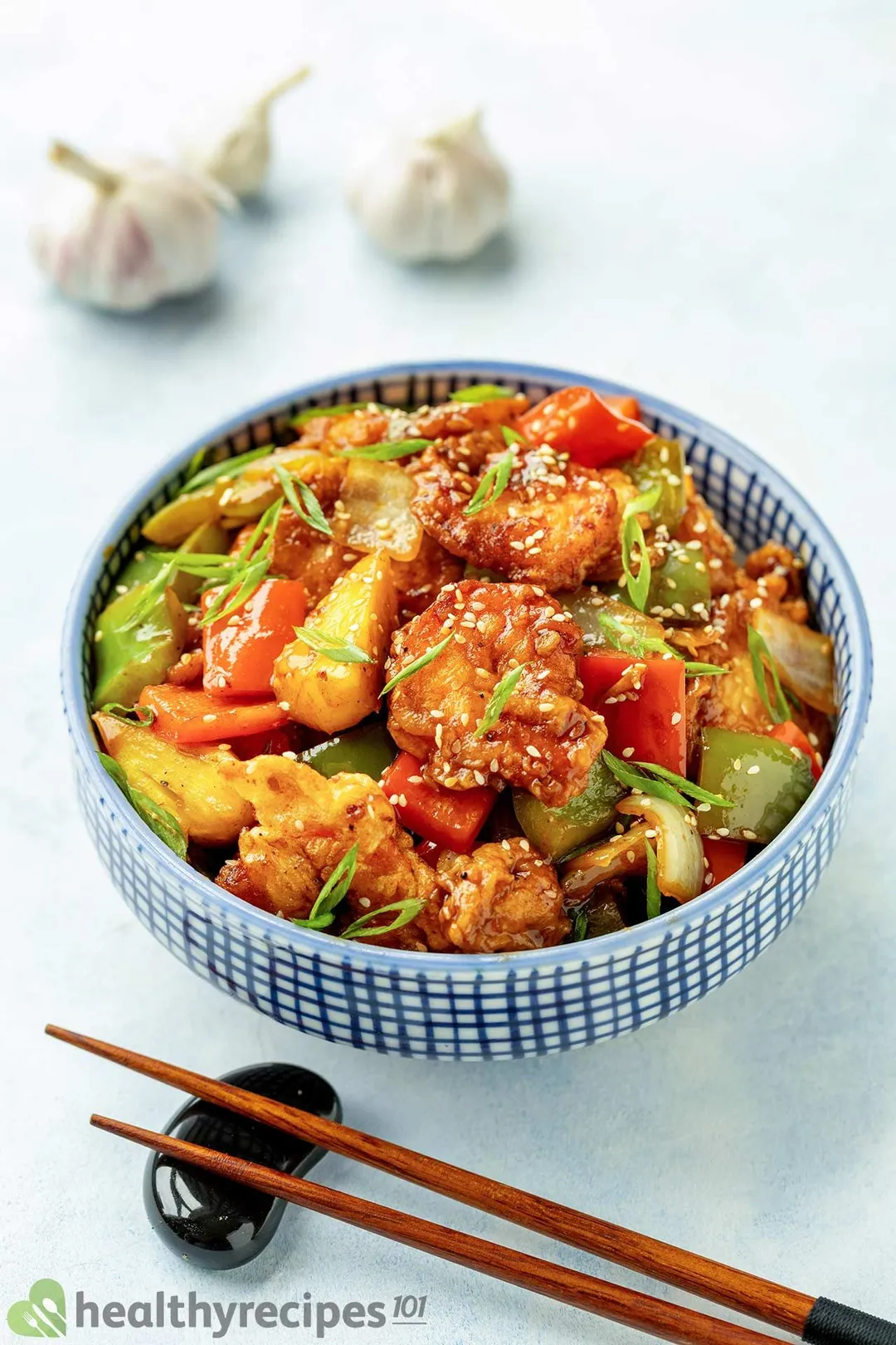 A stir-fry of battered shrimp and colorful vegetables in a cast-iron skillet, garnished with sesame seeds and scallions
