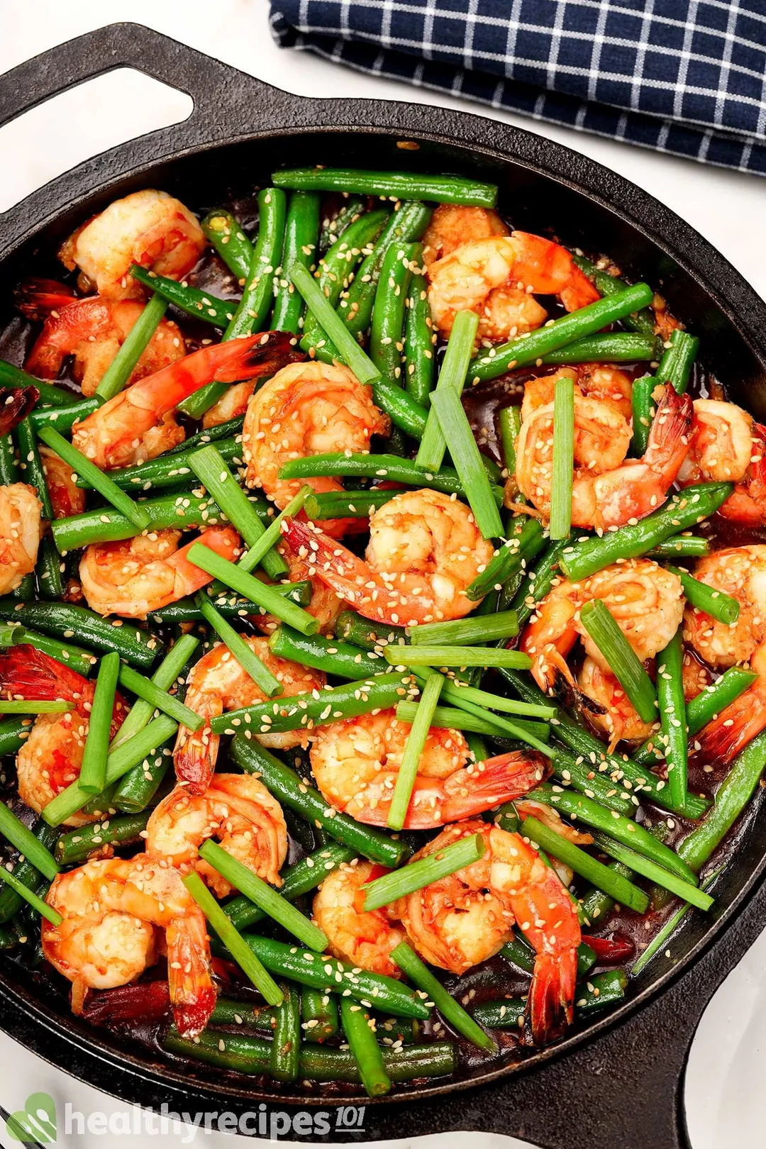 A close-up shot of red shrimp sauteed with green beans and sprinkled with white sesame seeds