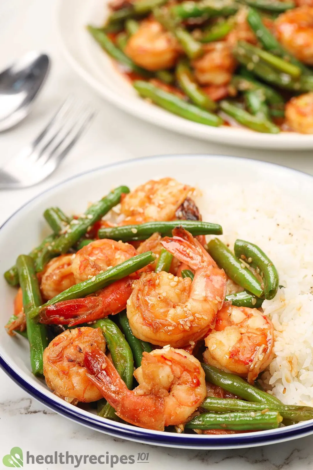a cast iron skillet of cooked shrimp sauteed with green beans and sprinkled with white sesame seeds
