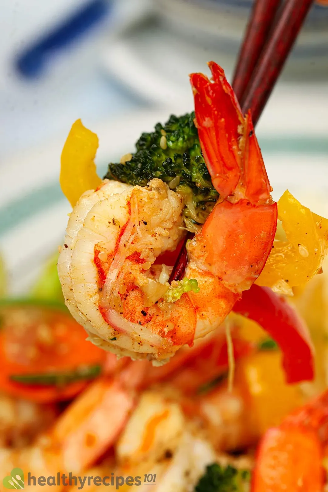 A close-up picture of sautéed shrimp, broccoli and bell pepper with a chopstick.