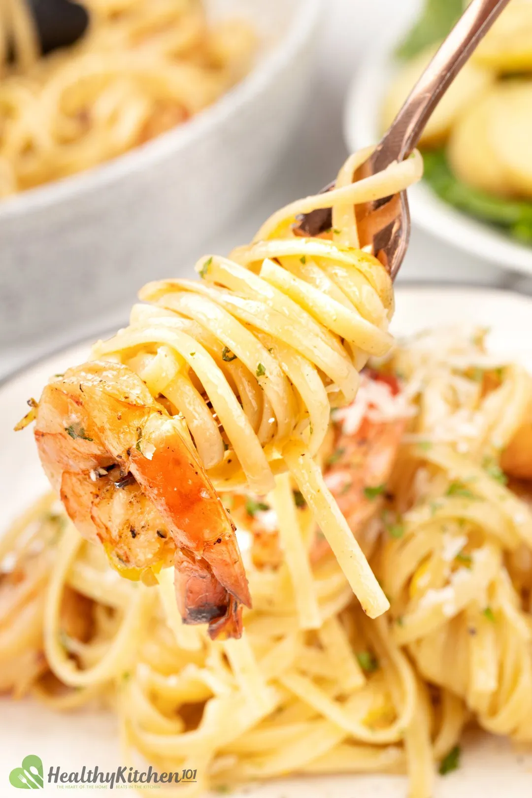 A close-up shot of fettuccine, shrimp, and shaved parmesan on top, with a salad in the background