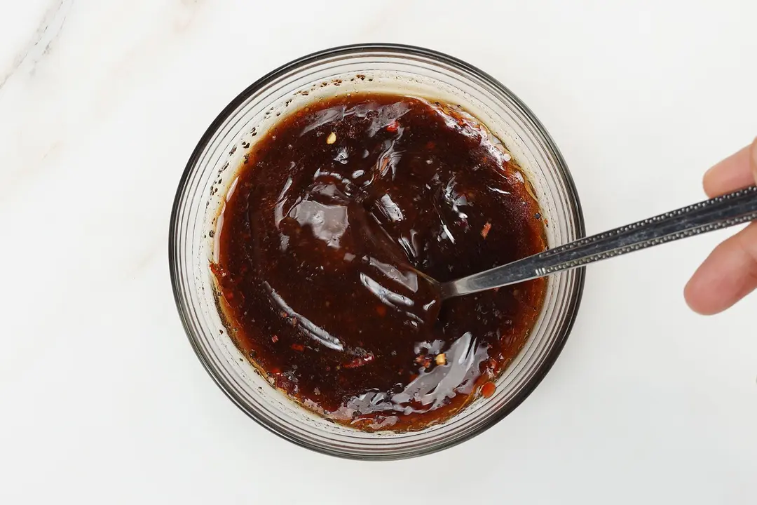 A small bowl of brown sauce being stirred with a metal spoon