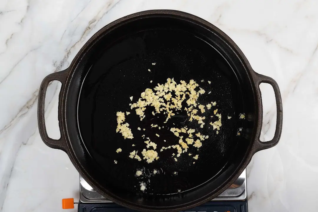 Minced garlic sizzling in the center of a cast-iron skillet