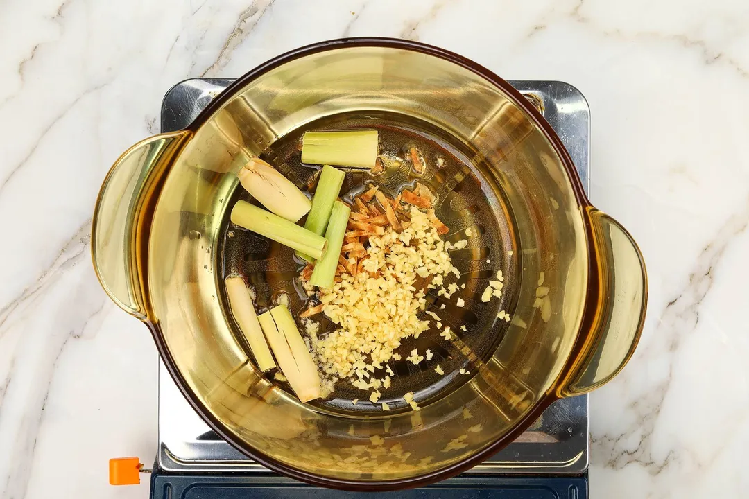 lemongrass, galangal and minced garlic in a pot on a stove