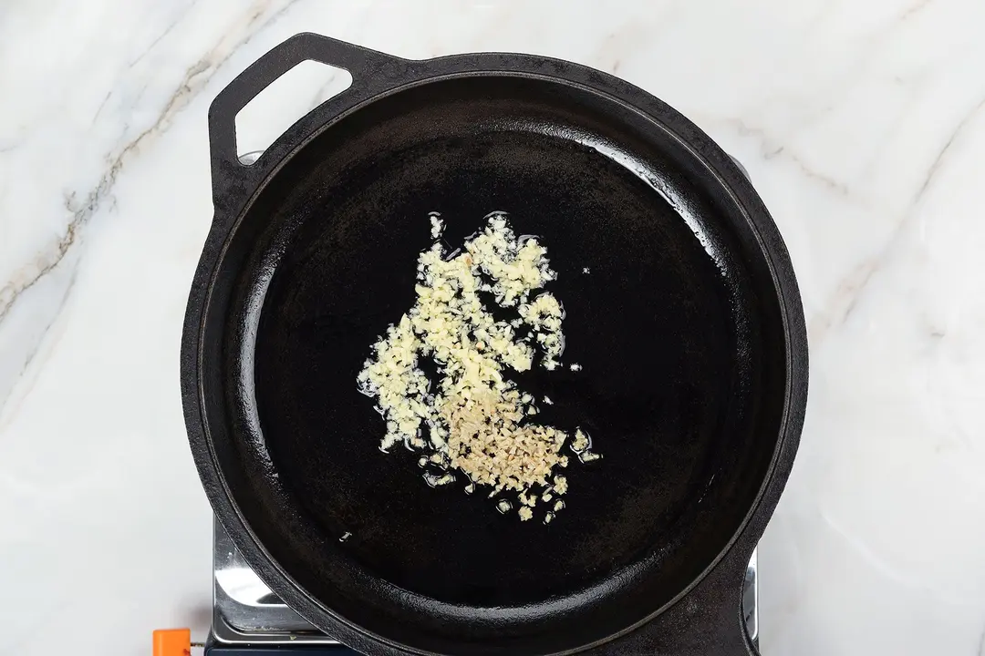 A black cast-iron skillet with chopped garlic sizzling in the center