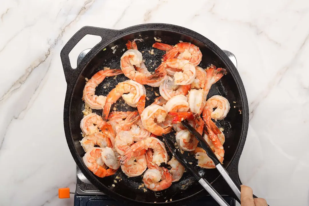 Shrimp stirred in a cast iron skillet with a pair of tongs to saute