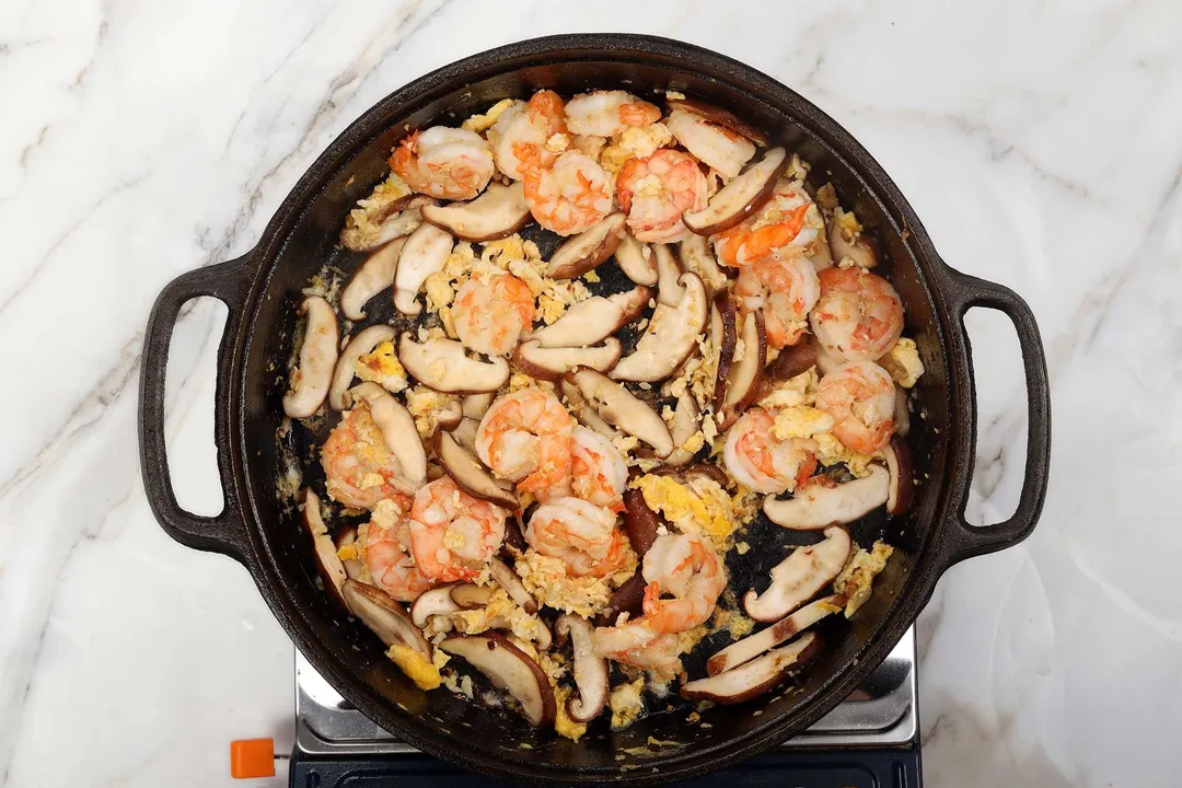 A saute of peeled shrimp, sliced mushrooms, and scrambled eggs in a cast-iron skillet