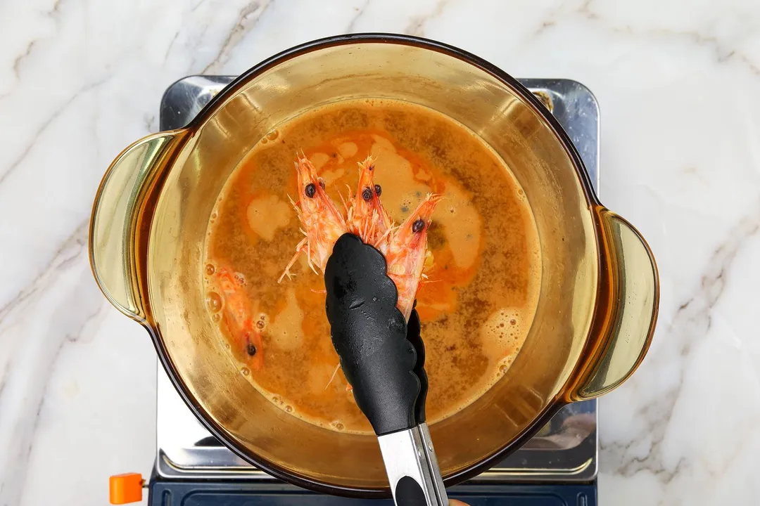 keeping 3 shrimp head by a tongs on top of a pot