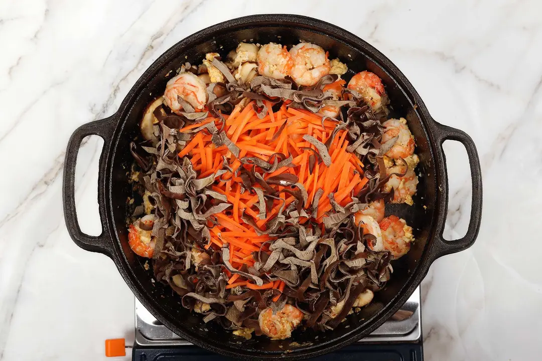 A cast-iron skillet full of julienned wood ears, carrots, and shrimps
