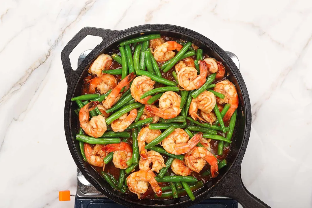 A cast iron skillet with cooked shrimp and green beans