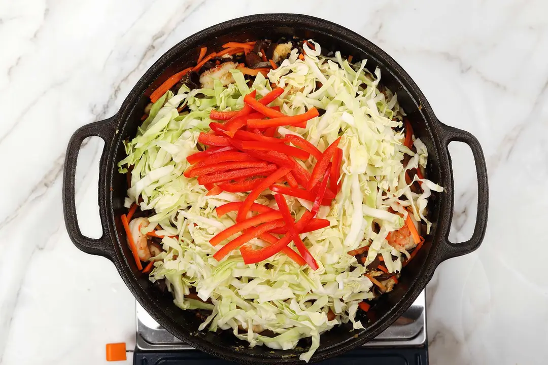 A pile of julienned pepper, cabbage, and other ingredients in a cast iron skillet