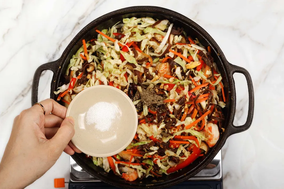 A small dish of salt hovering above a colorful saute held in a cast iron skillet