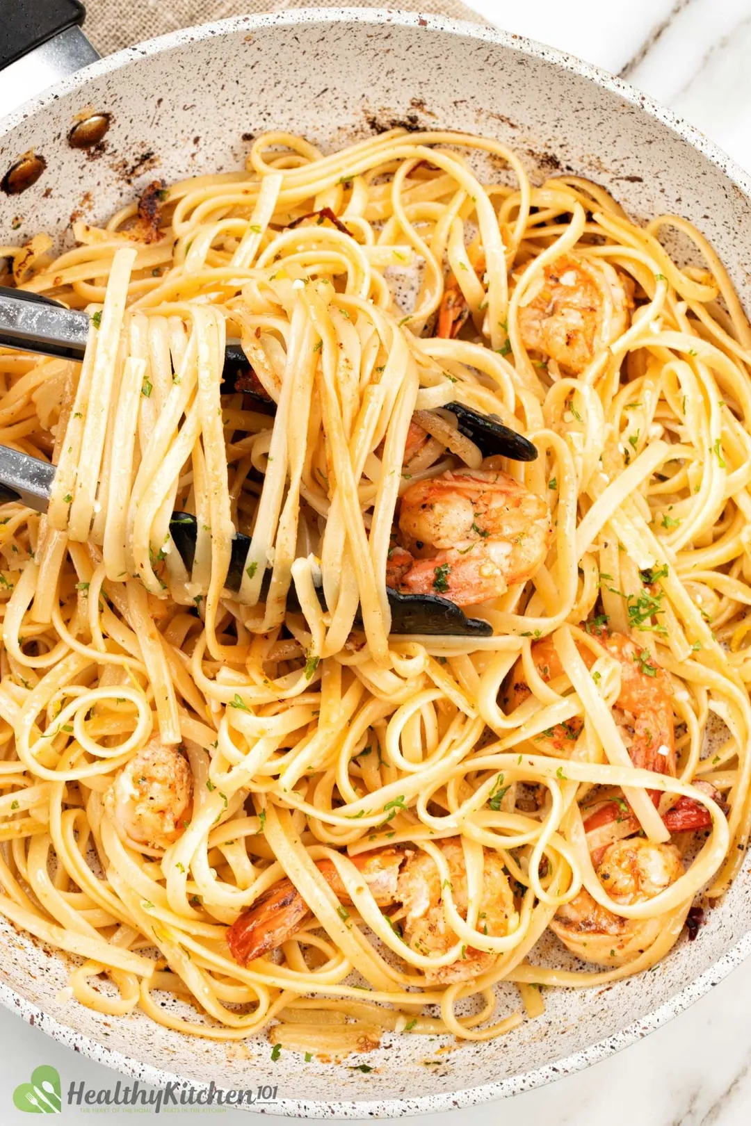 Shrimp fettuccine in a gray pan, with a black pair of tongs swirled in pasta on top