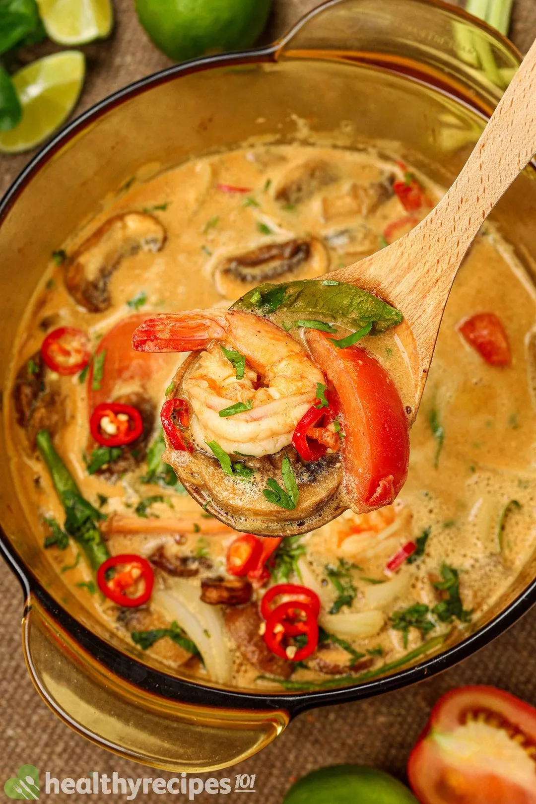 a wooden spoon full of shrimp tomato and lime leaves on top of a pot of soup