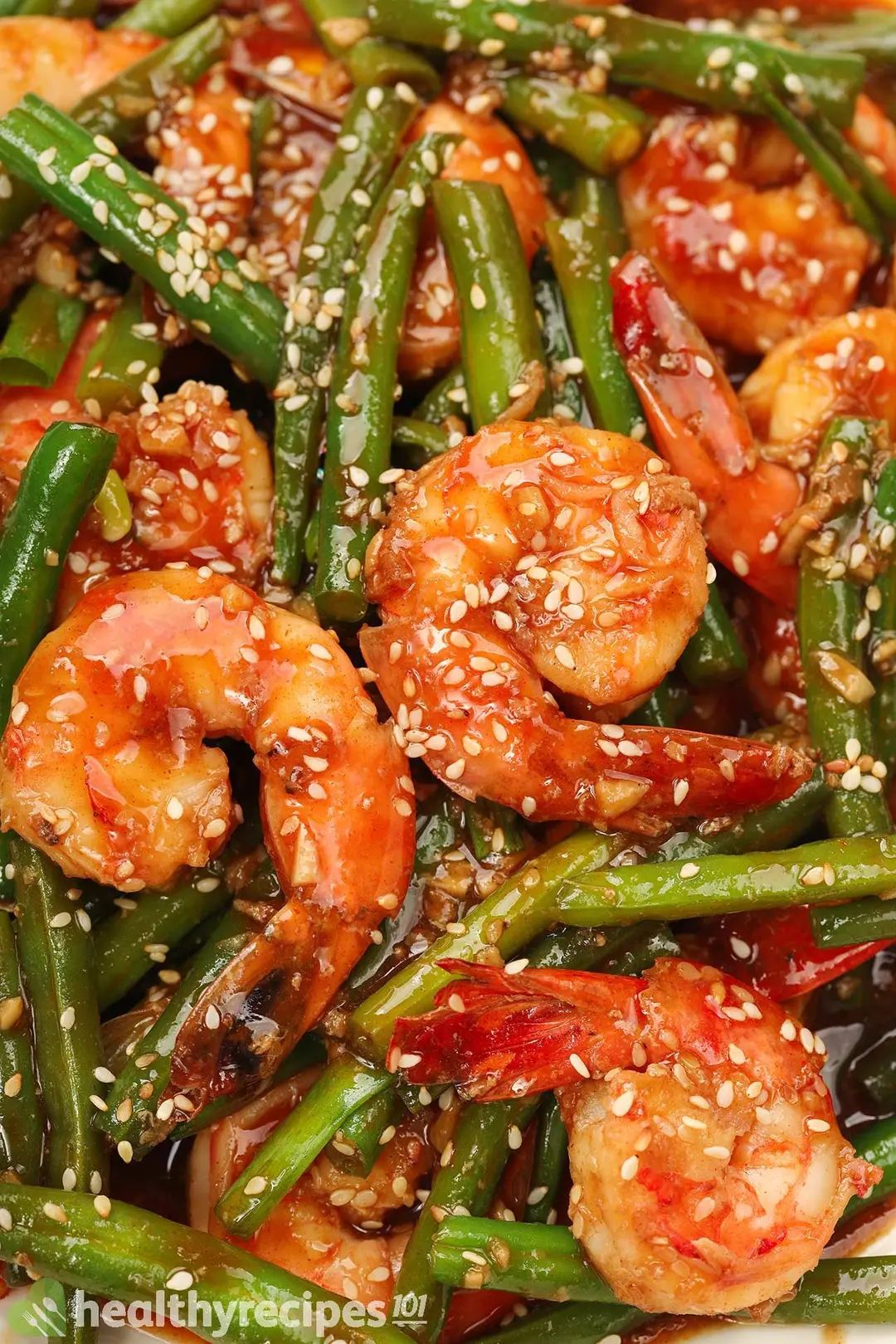 A plate of hunan shrimp sauteed with green beans served with cooked white rice, with a piece of blue checkered cloth in the background and other items