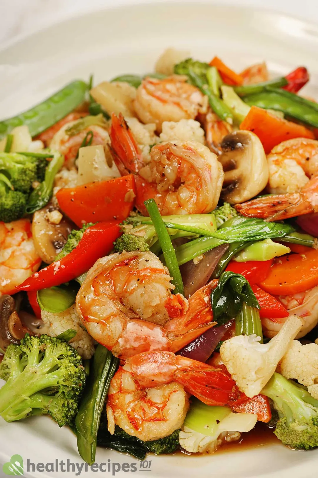 A spoonful of cooked shrimp, broccoli, pak choi, carrot, snow peas, red onion, and scallion.