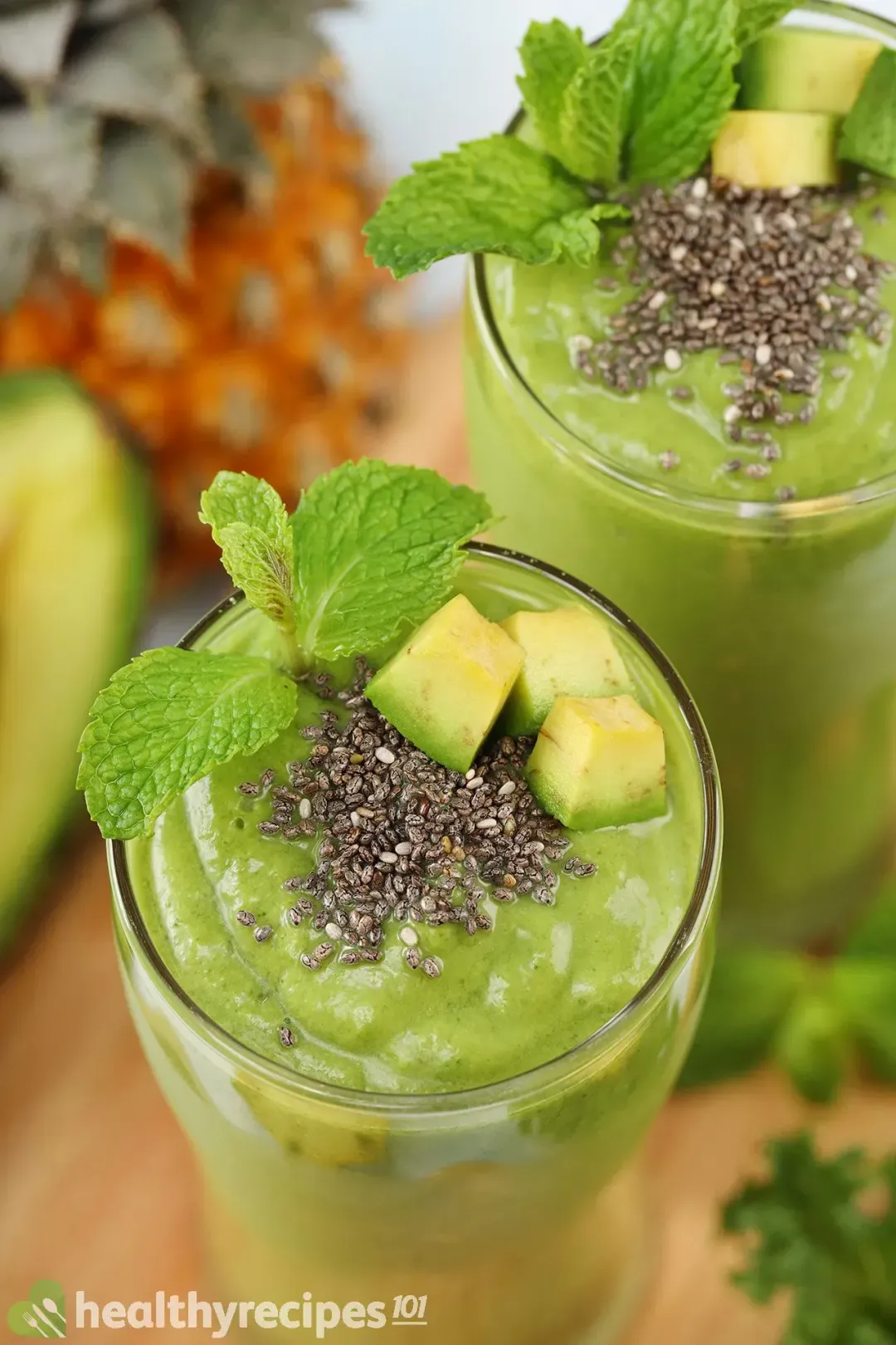 a glass of green smoothie on a wooden board with blueberries and blue-striped straws on the sides