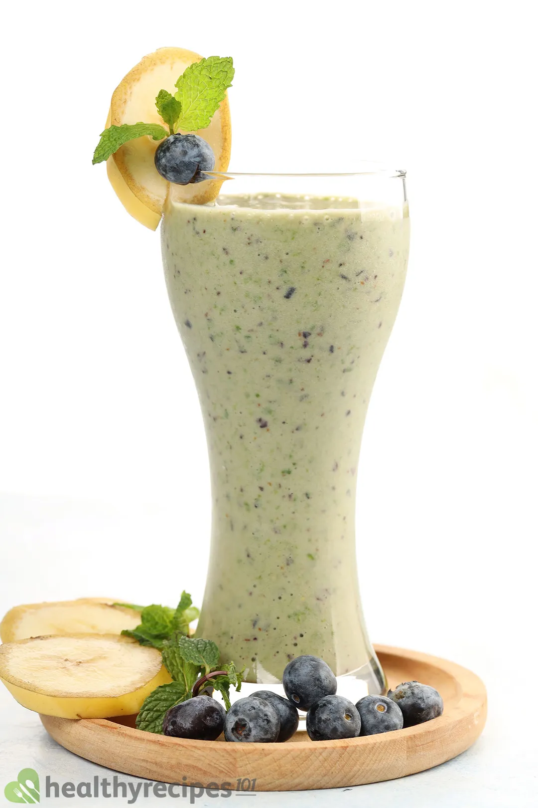 a glass of blueberry kale smoothie on a wooden tray, decorated with banana slices, mint and blueberries