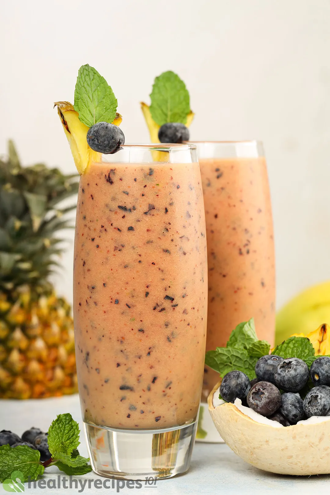 a glass of blueberry mango smoothie decorated by blueberries, pineapple and mint leaves