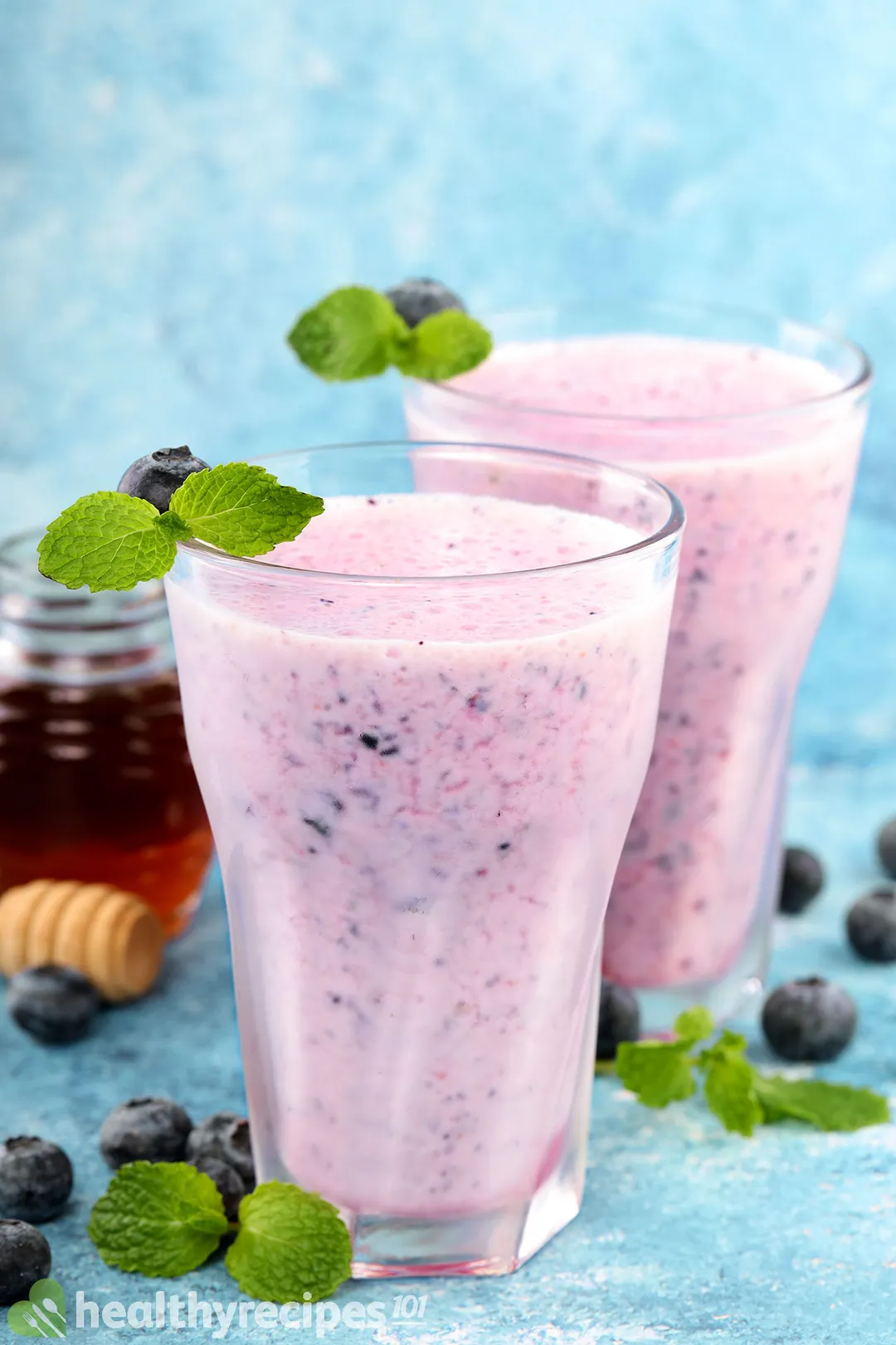 two glasses of blueberry yogurt smoothie decorated with honey jar mint leaves and bluberries