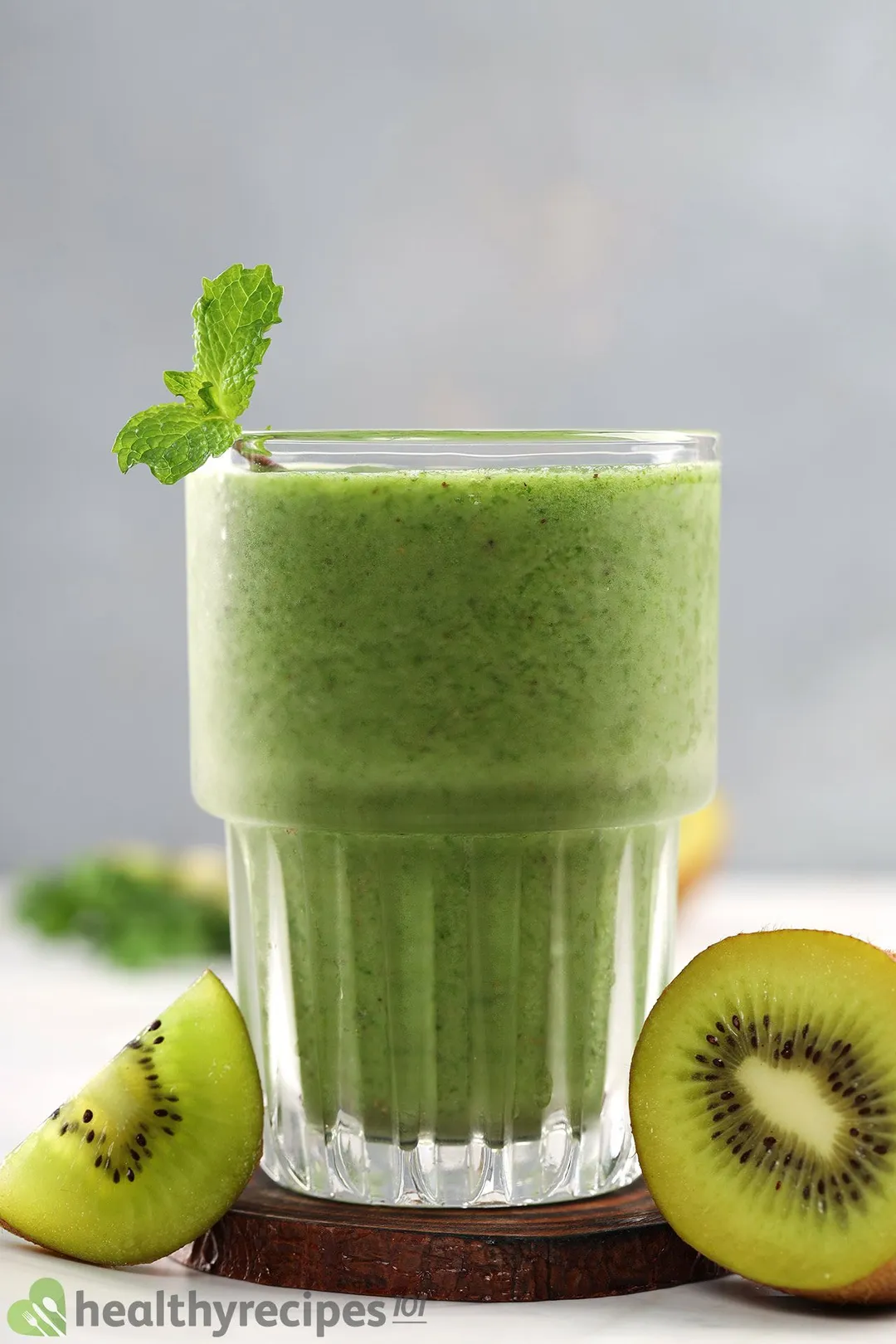 A green glass of apple kiwi kale smoothie placed on a wooden coaster and near sliced kiwis.