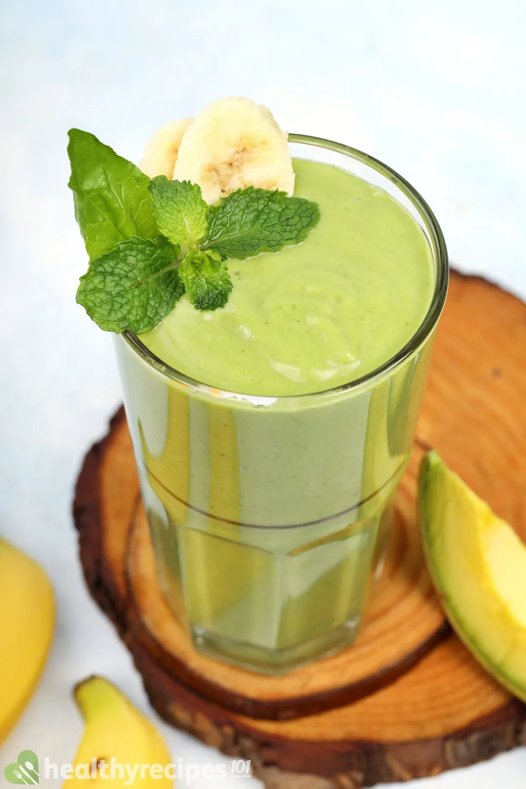 a glass of green smoothie on wooden tray with banana sliced and mint leaves on top