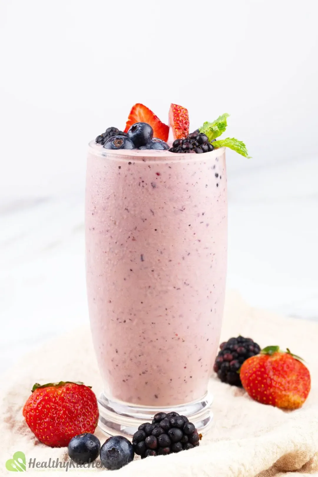 A glass of berry smoothie with vibrant berries on top and on the side