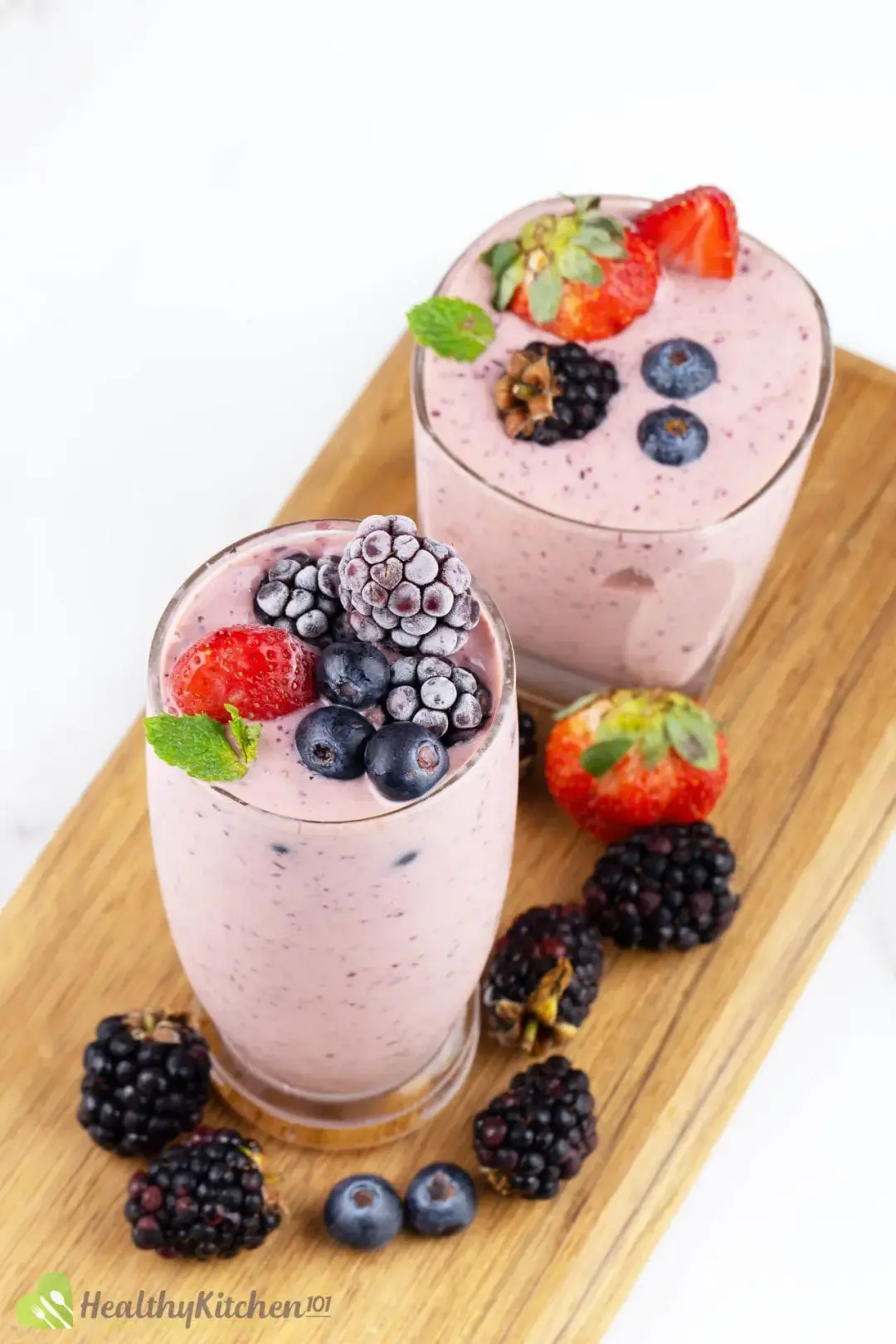 Two glasses of berry smoothie put on a wooden tray with berries around