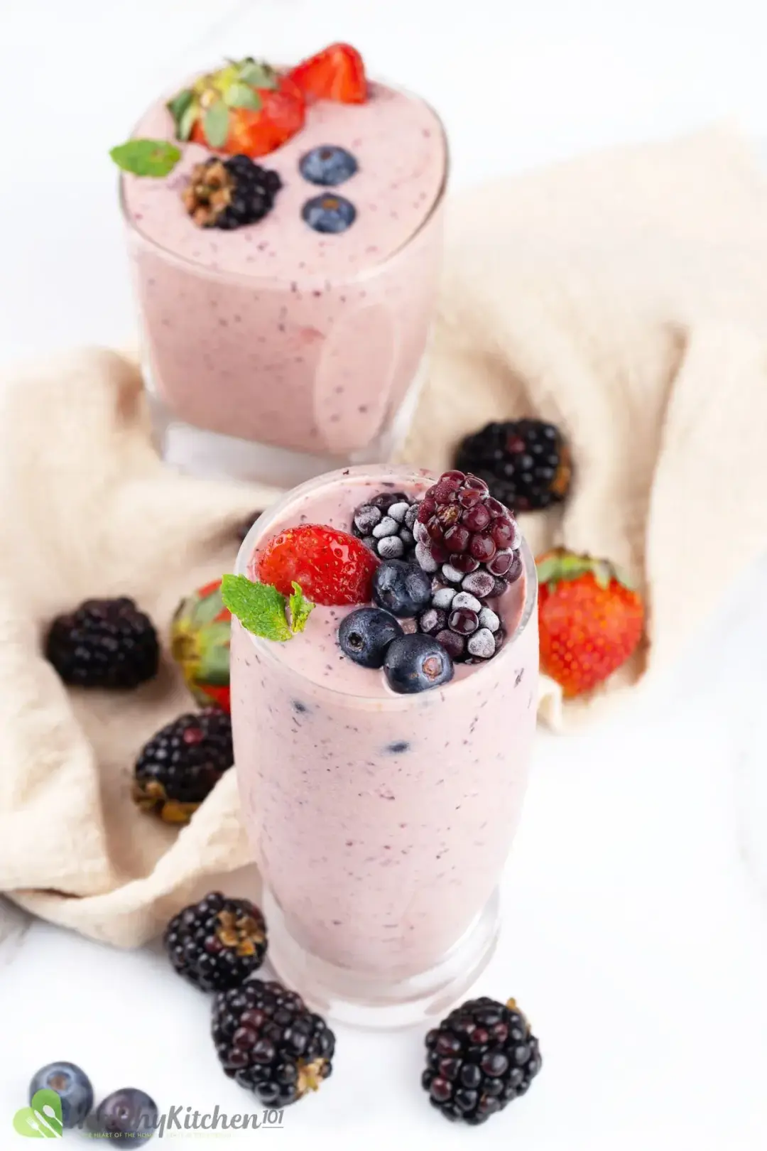 Two glasses of berry smoothies with colorful berries on top and around