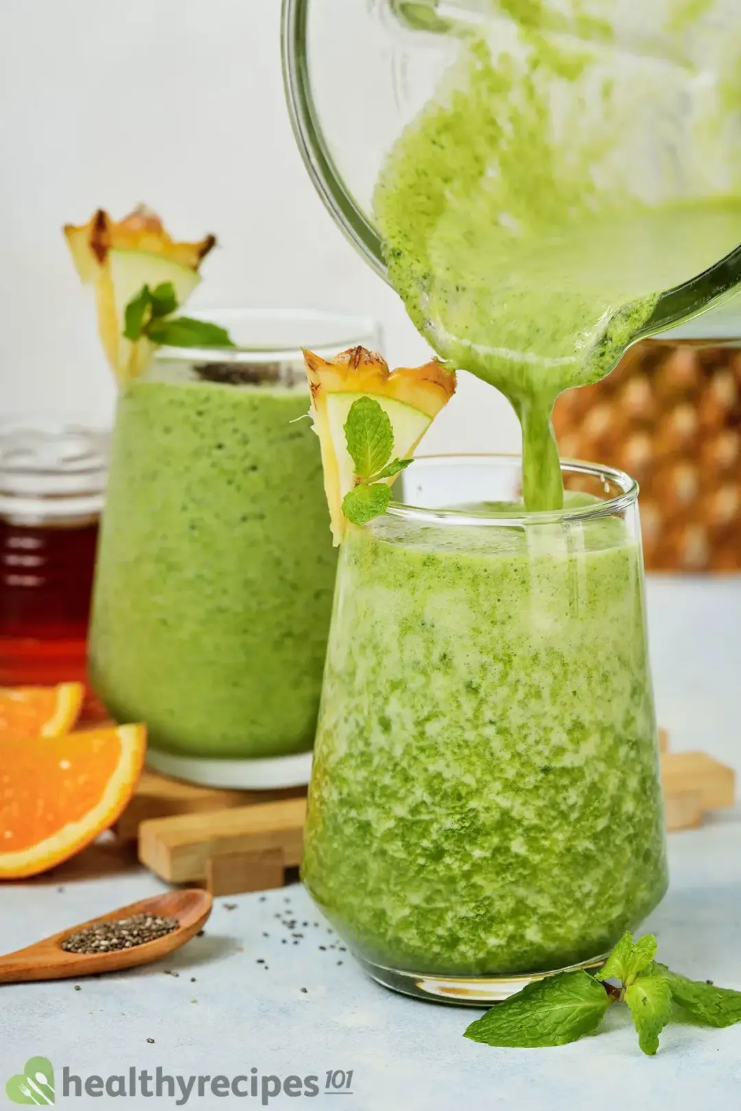 Two glasses of green apple smoothie, one of them is being poured from a blender