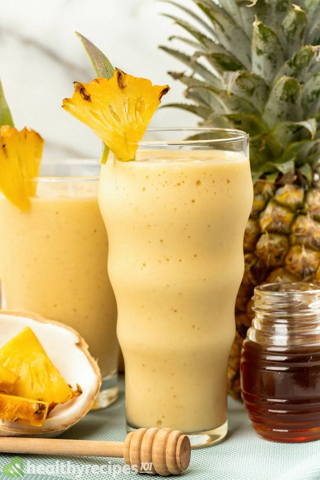 two glasses of pineapple smoothie decorated with pineapple, honey jar