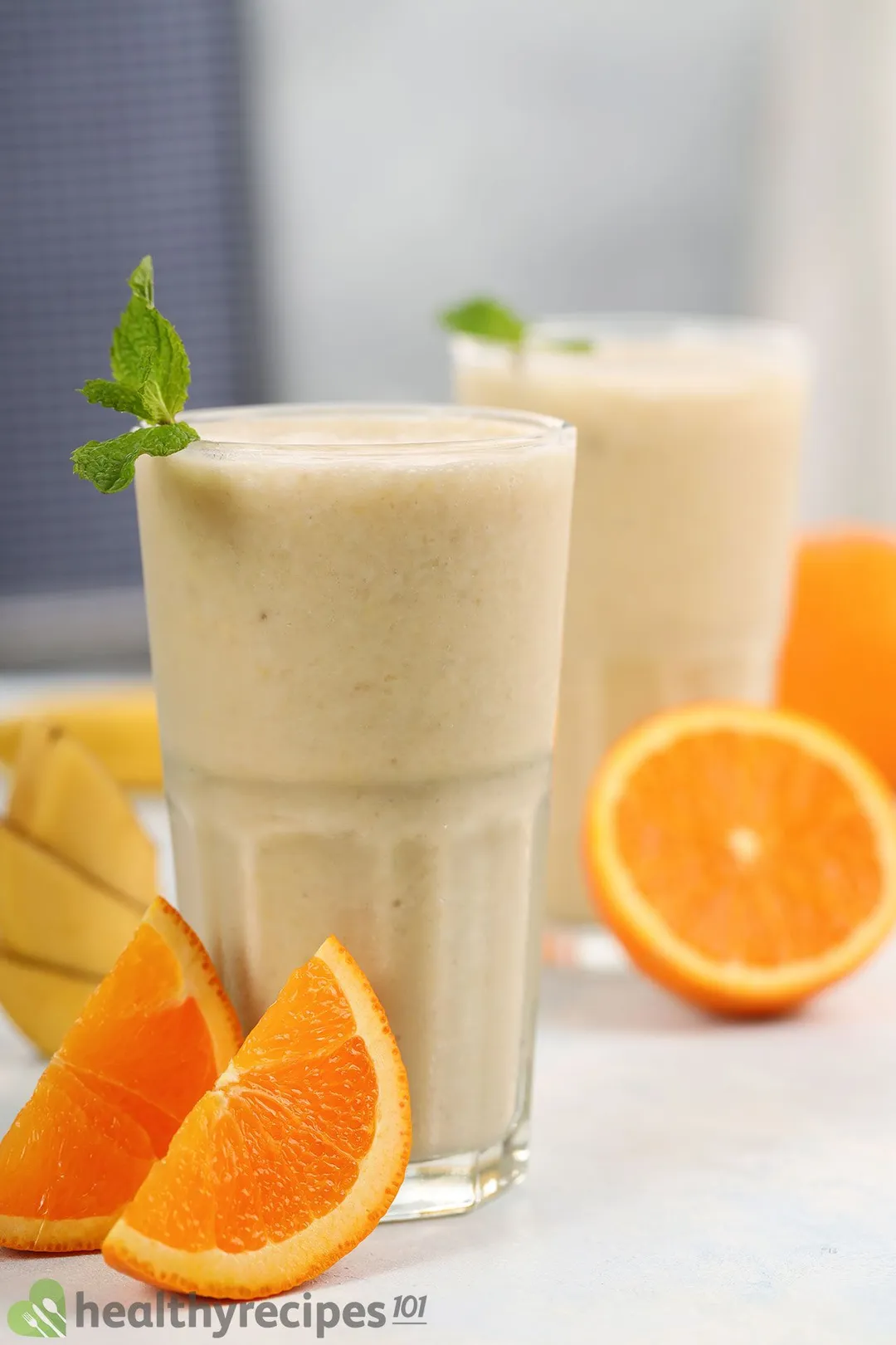 Two glasses of Orange Banana Smoothie placed near slices of orange.