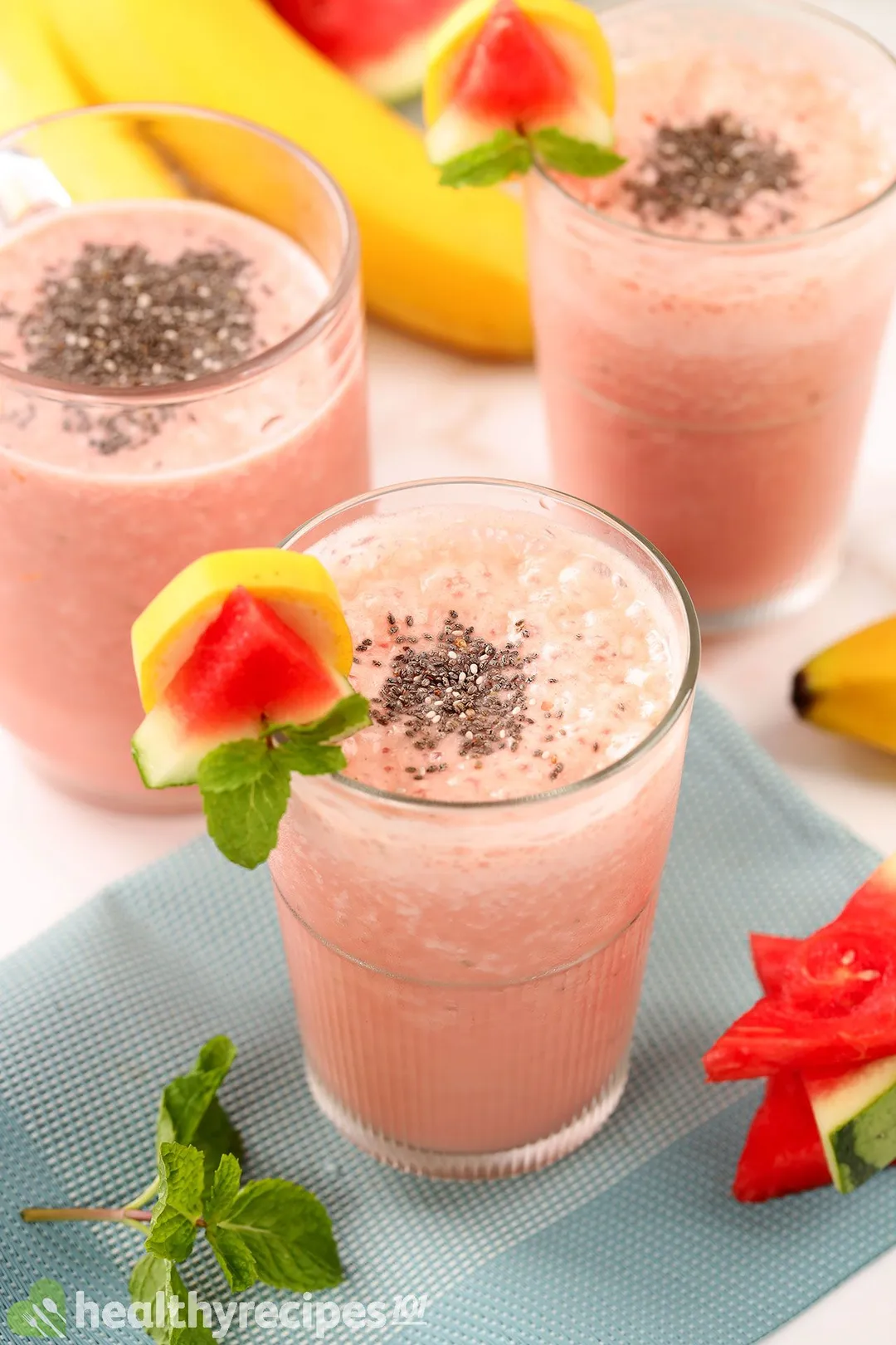 Three glasses of Watermelon Banana Smoothie placed near mint leaves, bananas, and watermelon slices.