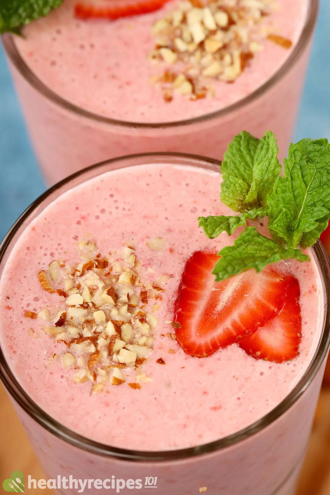 A high-angle shot of strawberry smoothie garnished with chopped almond, strawberry slices, and mint leaves.