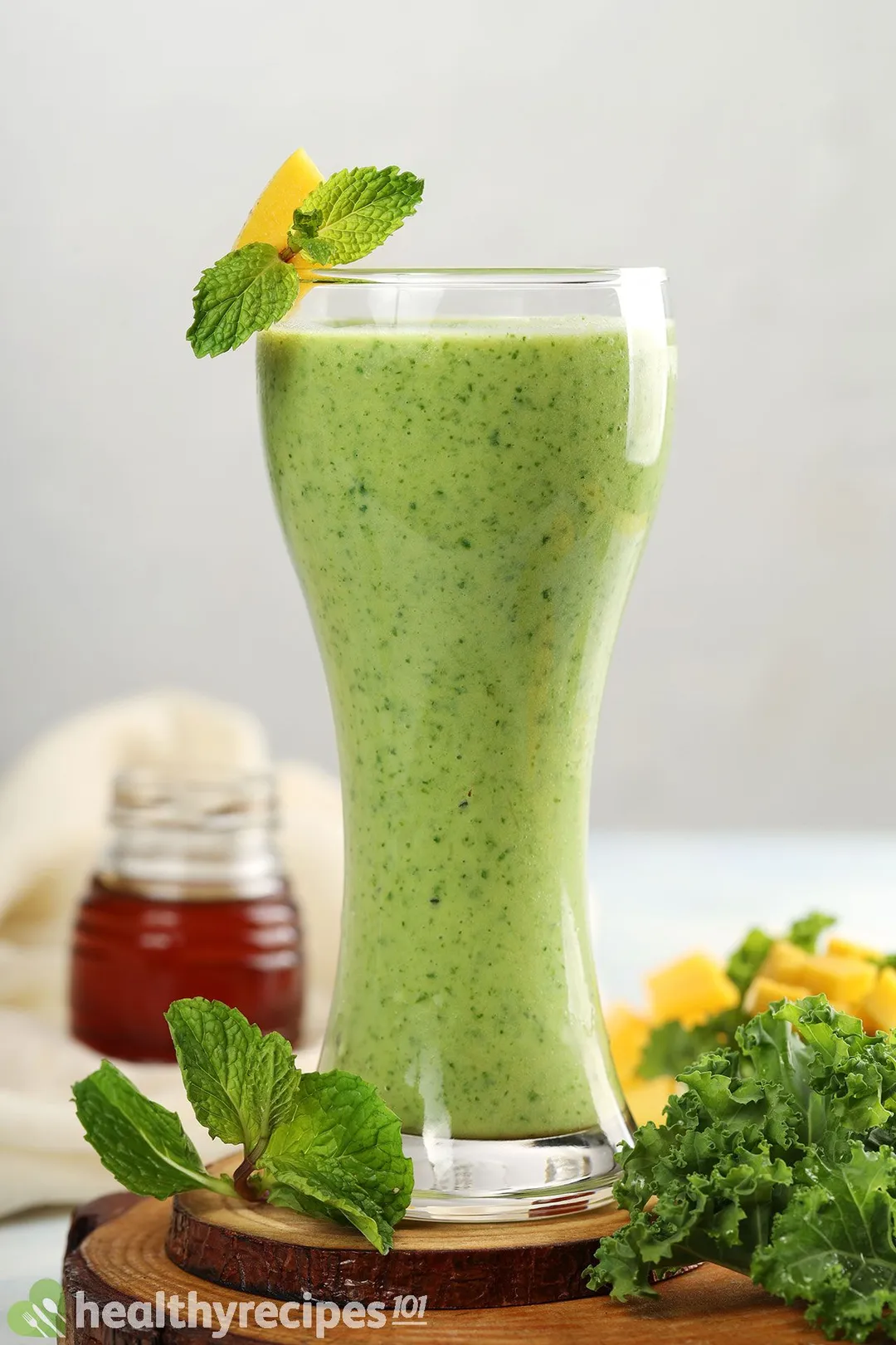 a glass of mango kale smoothie on a tray decorated with mint, kale and a honey jar