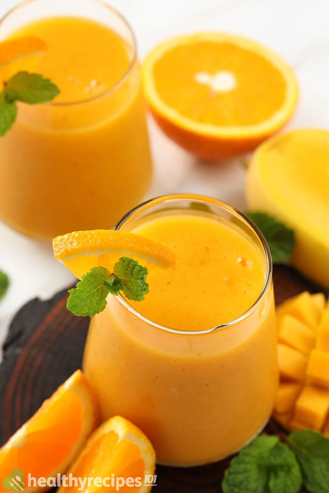 a glass of mango orange smoothie on a tray decorated with orange slices