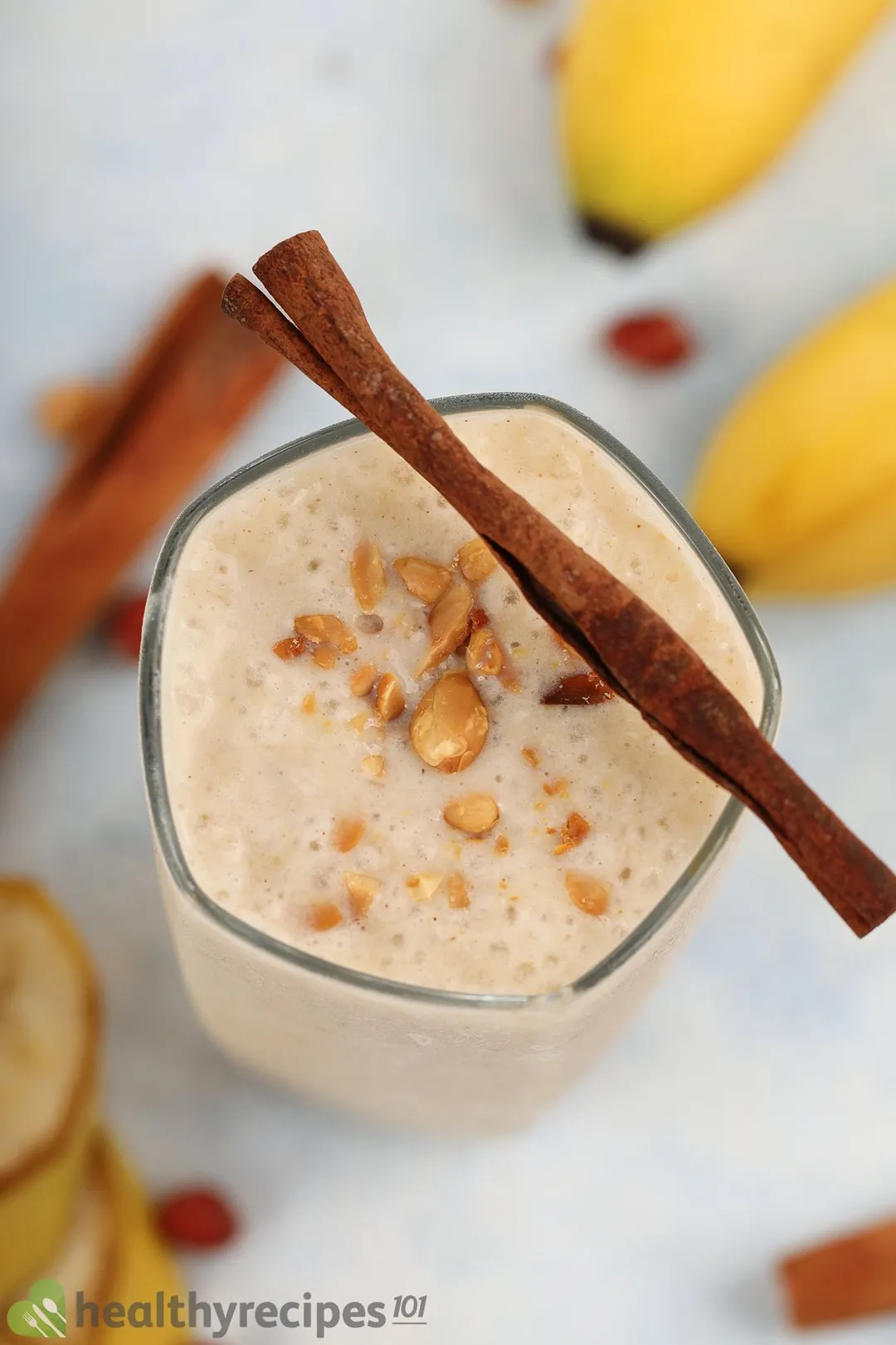 A high-angle shot of a glass of peanut butter banana smoothie garnished with a cinnamon stick and some peanuts.