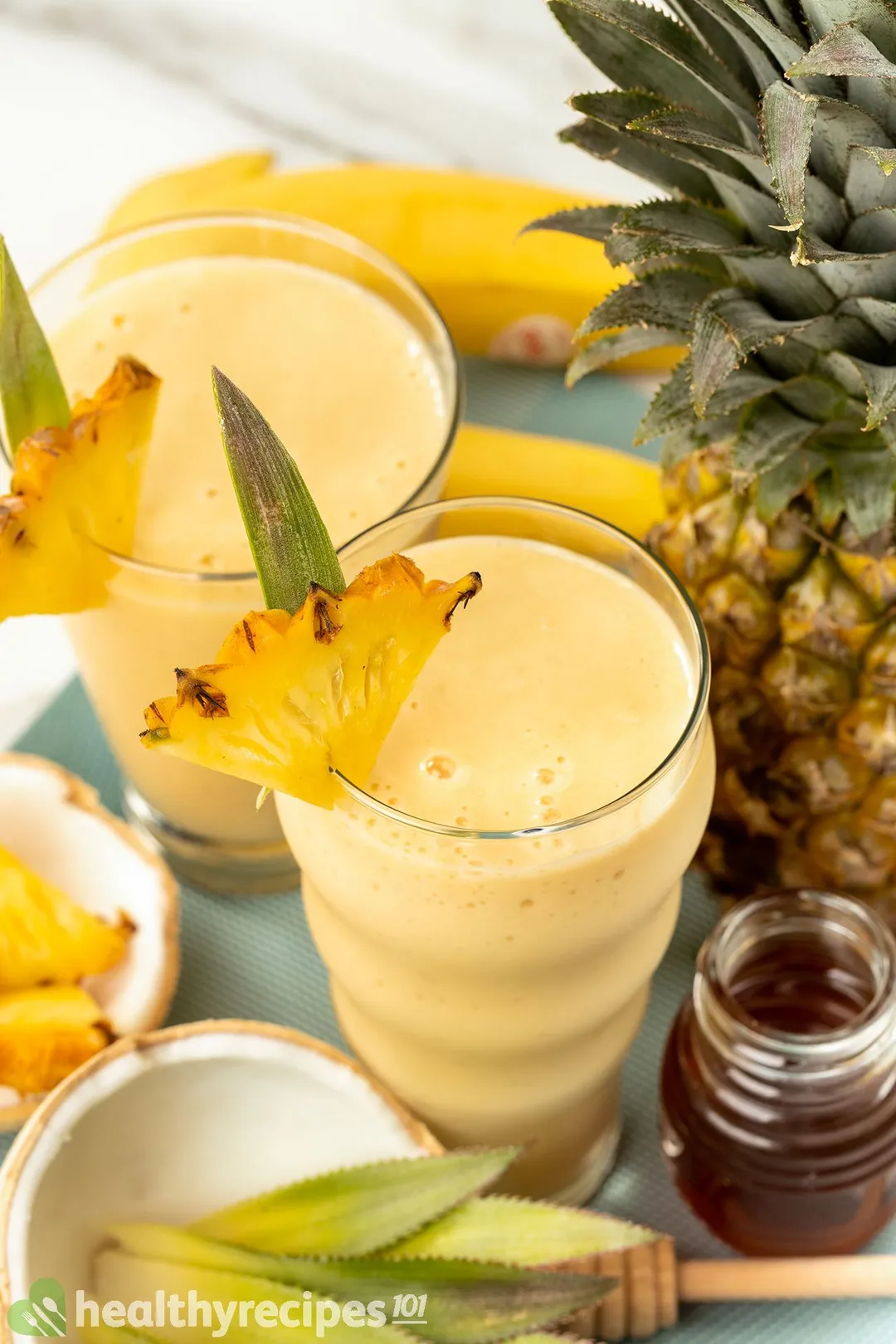 2 glasses of pineapple smoothie decorated with honey jar, a pineapple