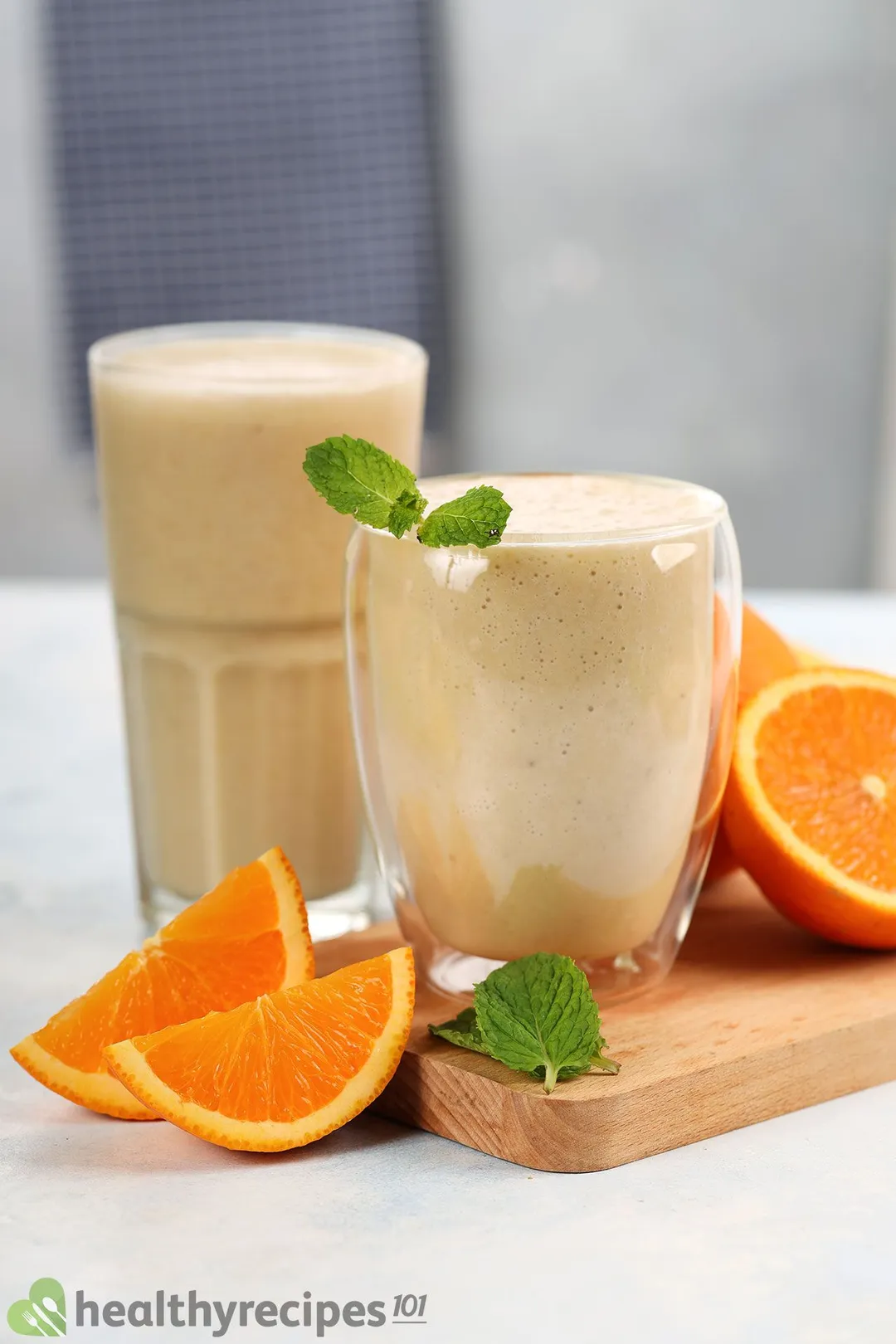 Two glasses of Orange Banana Smoothie placed on a wooden board and near orange slices.
