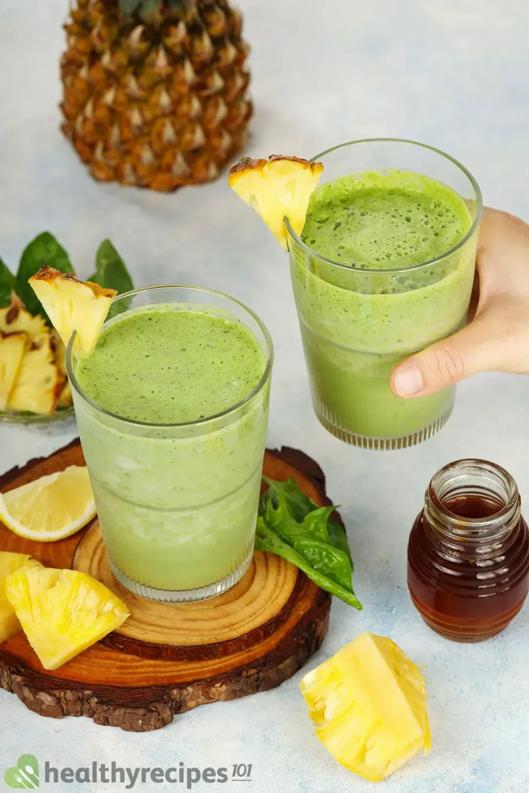 Two green smoothie glasses with pineapple wedges and lemon wedges and a honey jar
