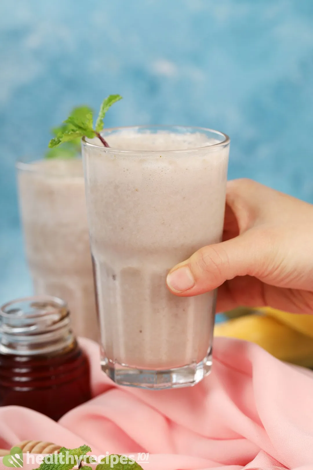 A hand picking up a glass of banana smoothie.