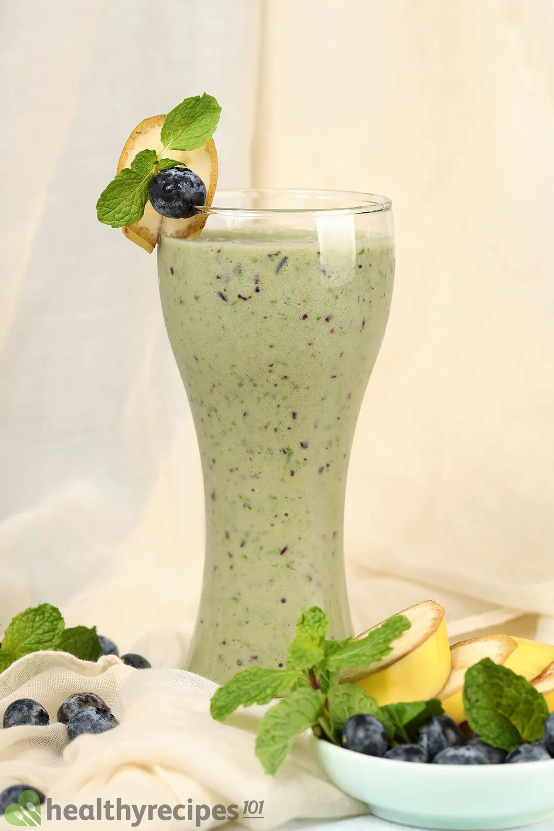 a glass of blueberry kale smoothie, decorated with blueberries, banana slices, mint leaves