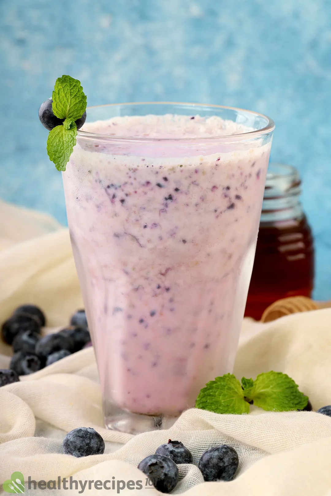 a glass of blueberry yogurt smoothie decorated with a honey jar, blueberries and mint leaves