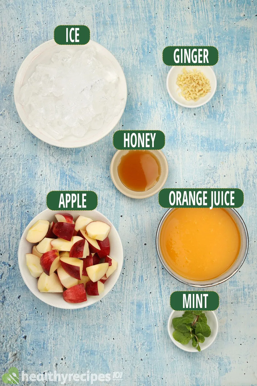 Ingredients for apple orange smoothie, including bowls of ice, sliced apples, orange juice, mint leaves, honey, and sliced ginger.