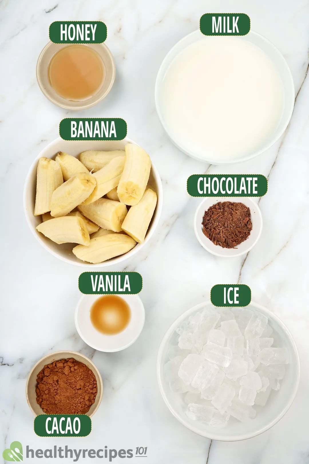 Ingredients for chocolate banana smoothie, including bowls of sliced bananas, cocoa, minced chocolate, ice, and other essentials.