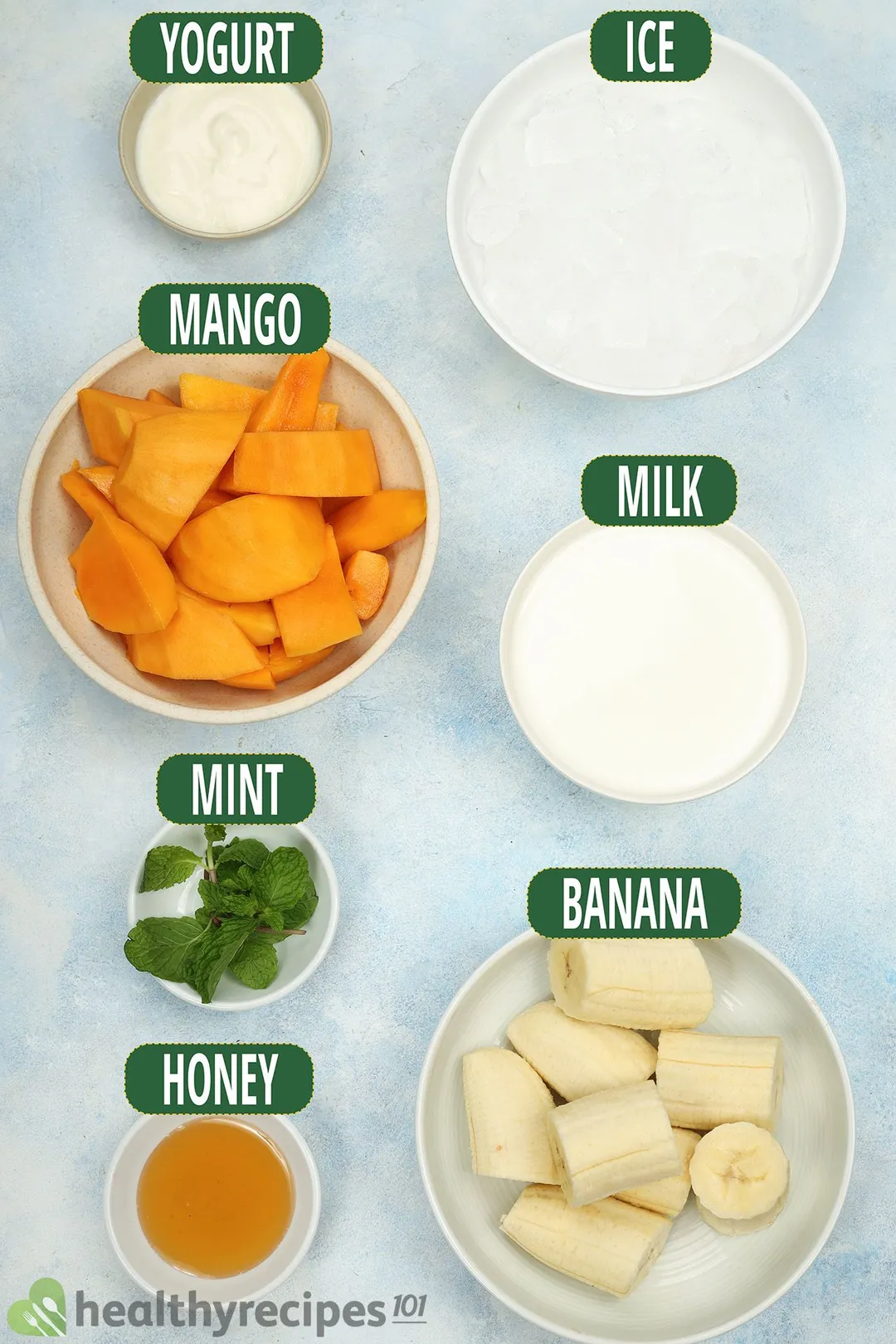 Ingredients for Mango Banana Smoothie, including bowls of mango slices, peeled bananas, ice, and other smoothie essentials.